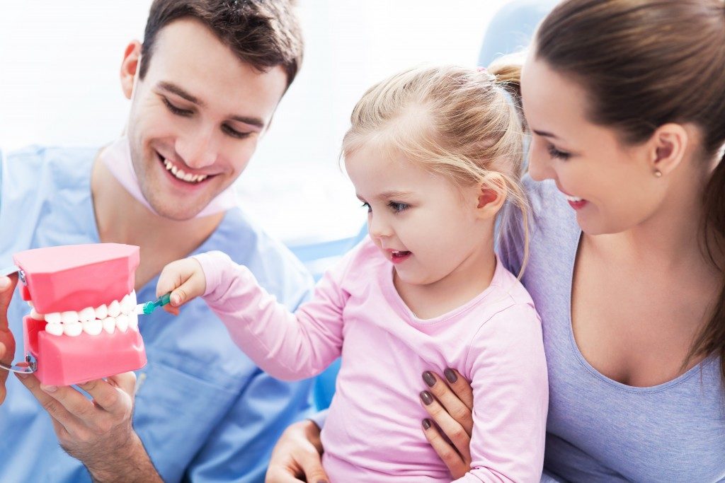 Dentist and parent teaching child how to brush teeth