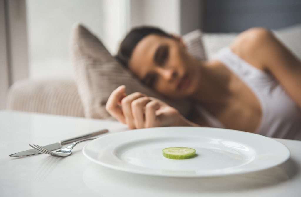 woman laying on the sofa looking dull staring at a piece of cucumber on the plate