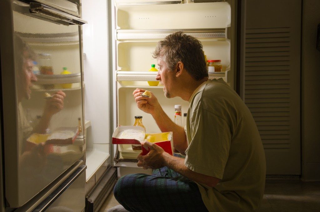 man eating late at night at the front of an open refrigerator