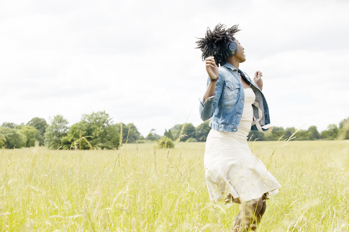 A woman dancing with headphones on in a meadow