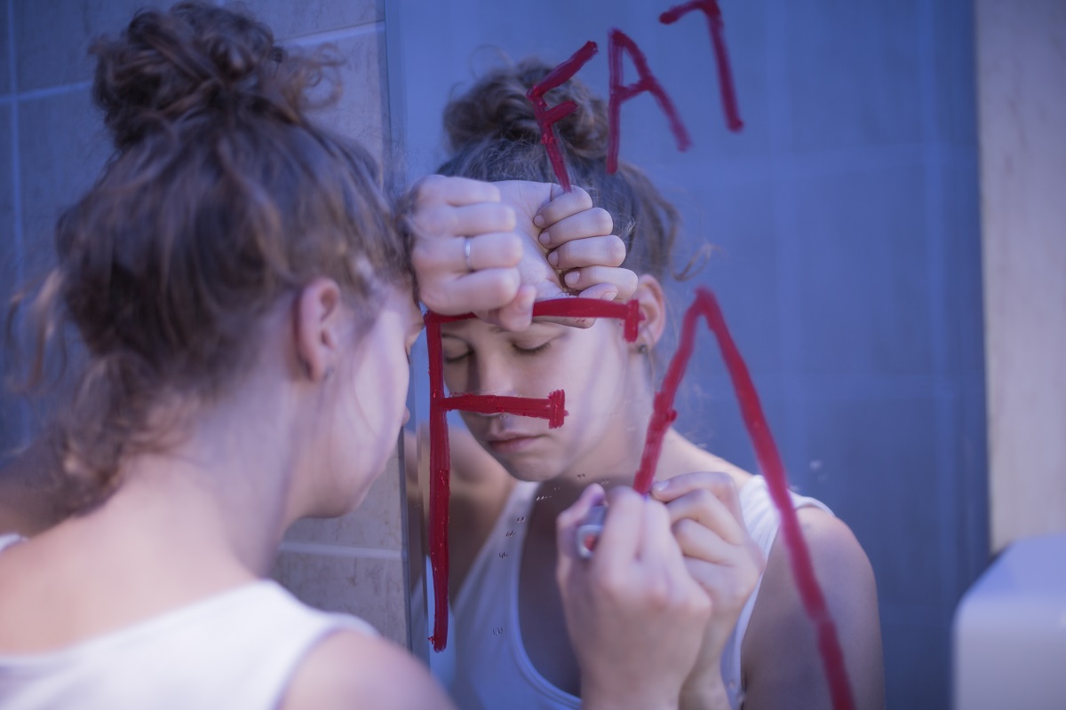 woman writing fat on the mirror