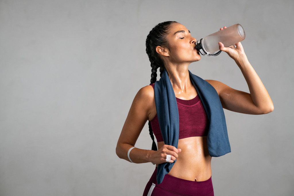 Young woman drinking water after exercising at a gym.